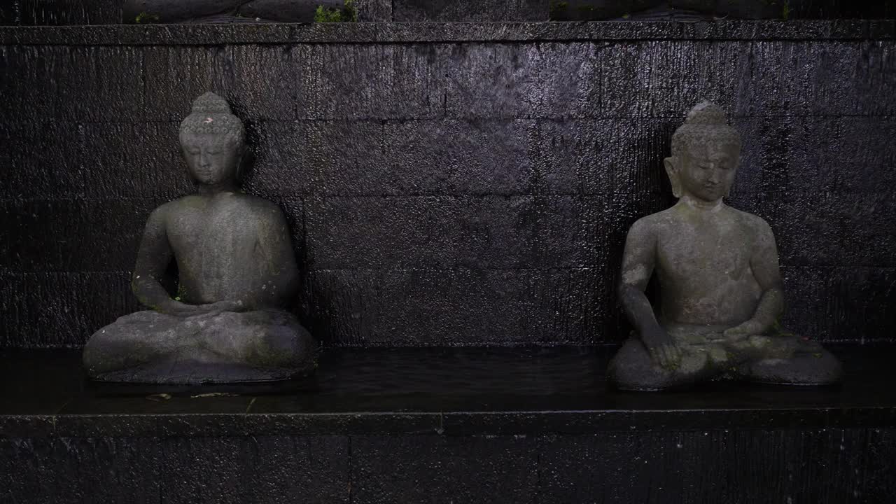 一尊佛像面对前方冥想，石墙背景上有瀑布。菩萨的脸。卫塞节和启蒙节的概念。空白复制文本空间视频下载