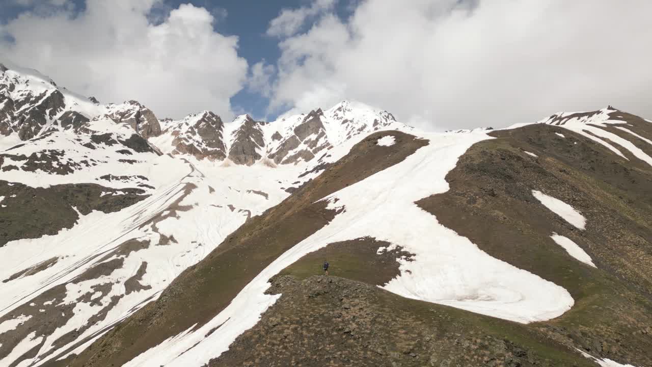 独自背包客伸开双臂，欣赏斯瓦涅季山脉的景色。孤独的旅行者在大自然中体验自由。冒险家在白雪皑皑的山峰，多云的天空。徒步旅行，探险，享受户外旅行。视频素材