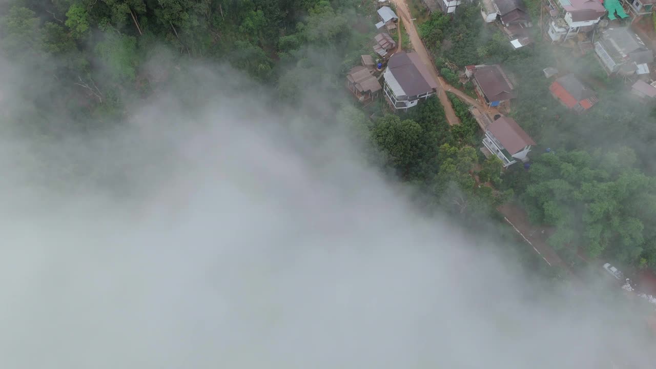 航拍照片捕捉了一个薄雾笼罩的山村，周围是郁郁葱葱的绿色植物和蜿蜒的道路，营造出宁静祥和的氛围。视频下载