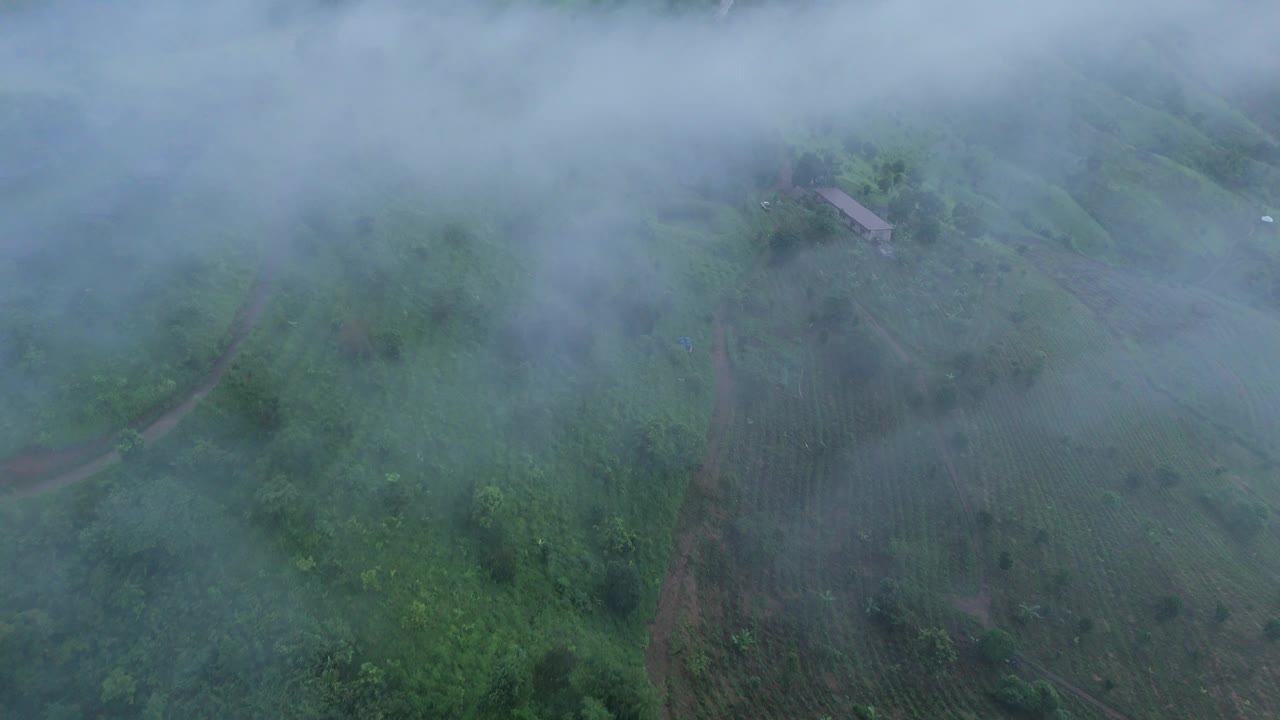 一个令人惊叹的鸟瞰宁静的山村坐落在郁郁葱葱的绿色山丘，迷雾的云增加了一个神秘的触摸景观。视频下载