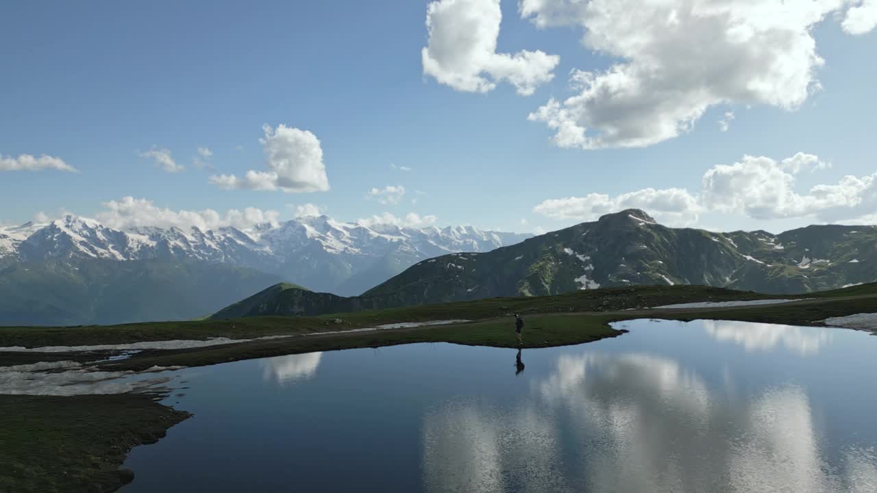 背着背包的徒步旅行者在Svaneti山脉的Koruldi湖边散步。鸟瞰白雪皑皑的山峰，碧绿的山谷，晴朗的天空。探险旅行、徒步旅行、自然风光、人在荒野、徒步小径。视频素材