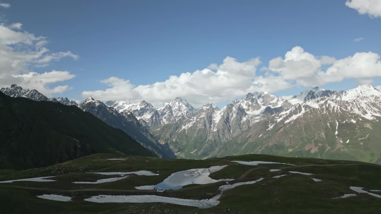 鸟瞰图:背着背包的徒步旅行者在被斯瓦涅季山脉环绕的Koruldi湖上。人们探索雪峰、青山、宁静高山景观的无人机。冒险，自然，旅行。视频素材