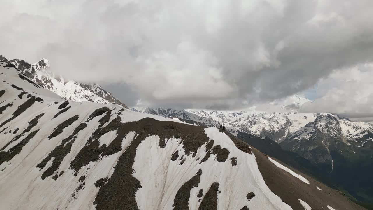 斯瓦涅季山脉的鸟瞰图，山顶被雪覆盖，天空多云。两个徒步旅行者沿着偏僻荒野的山脊行走。令人惊叹的景观是旅行，冒险，自然，旅游，徒步旅行的完美选择。视频素材