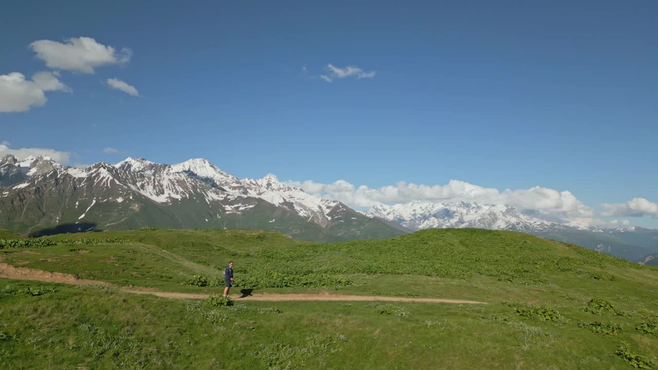 在斯瓦涅季山脉的高山草地上徒步旅行的男子鸟瞰图。独自旅行者走在风景秀丽的小路上，周围是宁静的风景。抑郁，孤独，冒险，探索的概念。无人机拍摄的视频素材