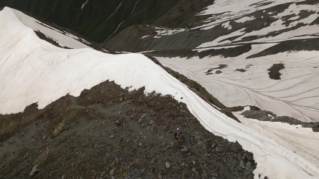 在雪山中背着背包登山的鸟瞰图。在山峰附近的岩石地形上跋涉的人。冒险徒步旅行，探索大自然。积极休闲，户外探险。无人机拍摄的视频素材