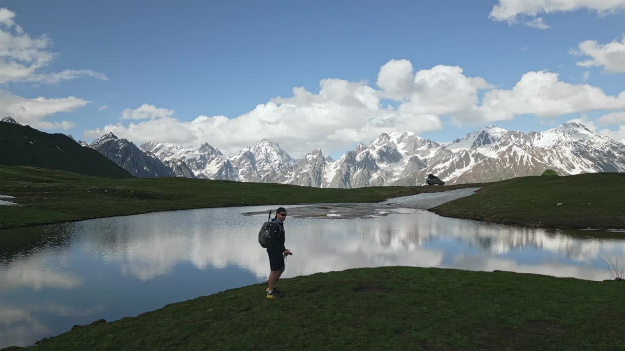 背着背包的徒步旅行者的空中无人机。在斯瓦涅季山脉Koruldi湖边散步的人。雪峰、蓝天、山水、静水。徒步生态旅游、探险旅游。无人机视频素材