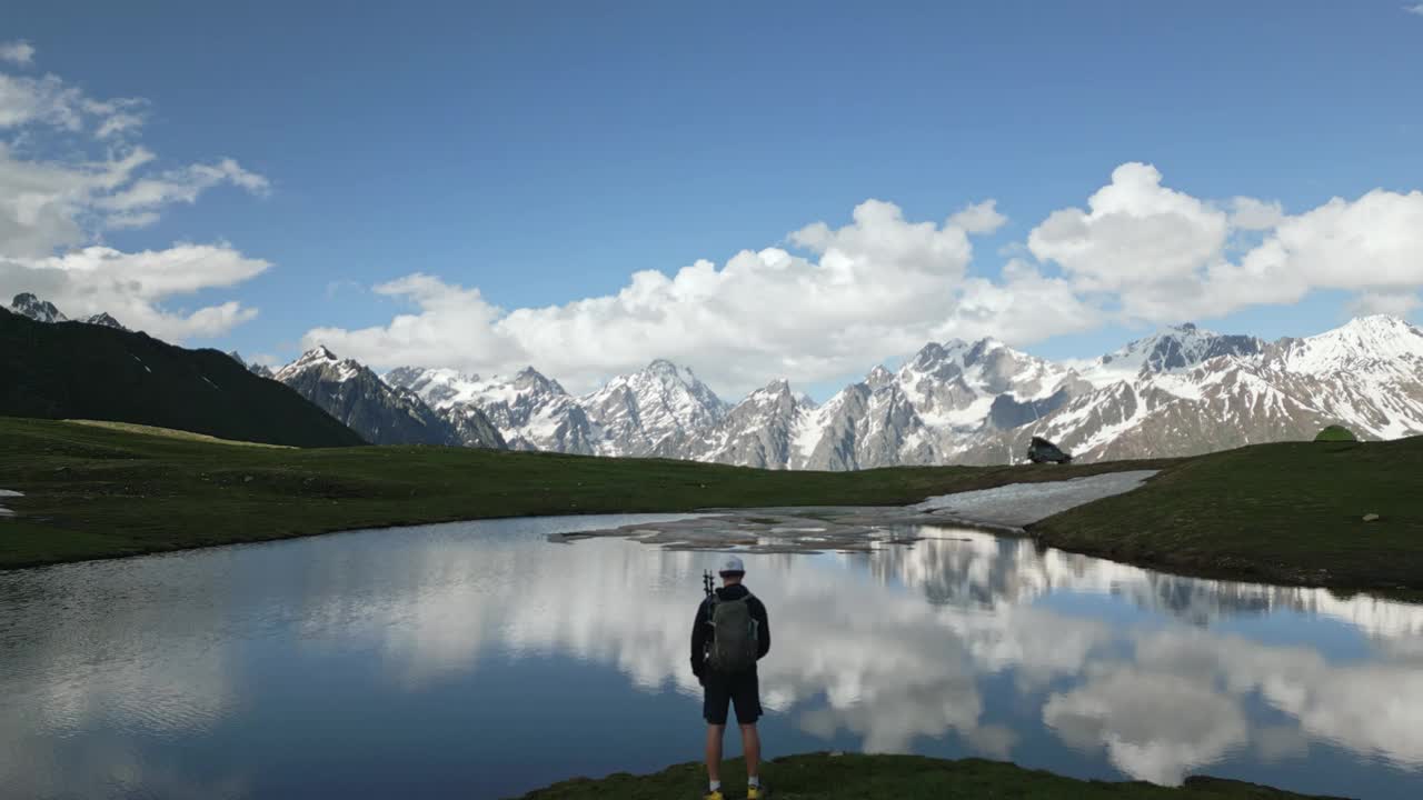 背着背包的徒步旅行者探索Svaneti山脉的Koruldi湖。鸟瞰图的人旁边的湖泊和雪峰。冒险家在乔治亚州徒步旅行。印象中的荒野，遥远的旅行目的地。视频素材