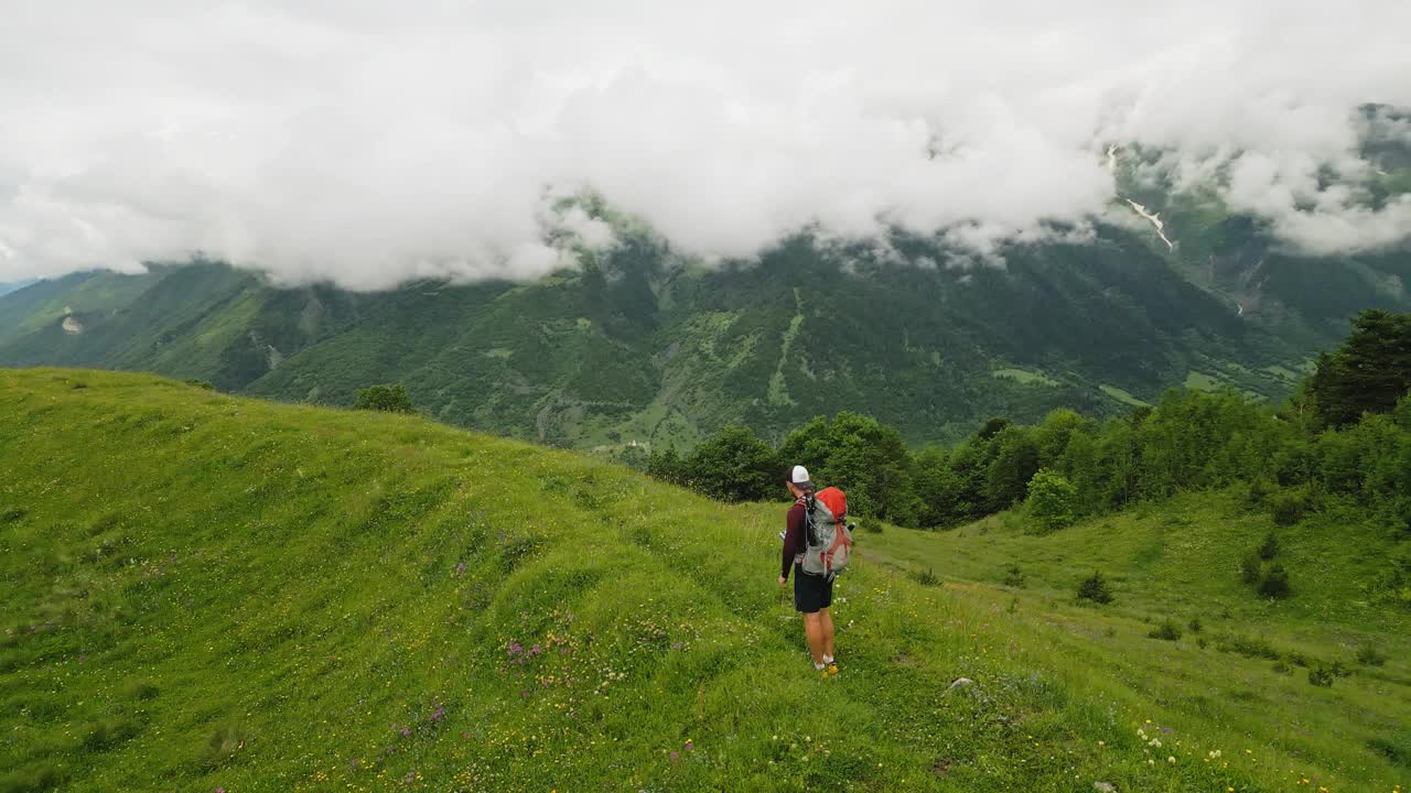 独自旅行者背着背包徒步穿越高山草甸，享受大自然。探索风景，绿色的山丘，多云的山脉。享受冒险，自由在野外高山景观，夏季远足径。视频素材