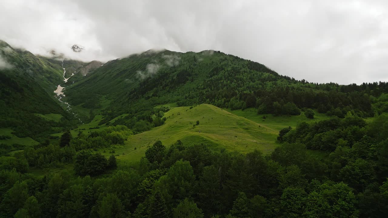 男子徒步穿过群山环绕的高山草地。冒险家探索自然，享受自由，呼吸新鲜空气。鸟瞰美丽的风景，强调旅行、户外活动、独处。视频素材