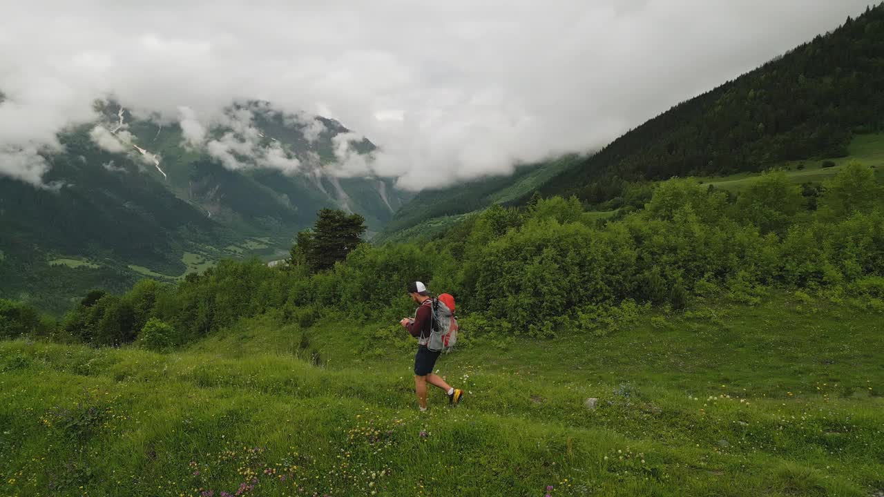 云天里，一个背着背包的人在长满绿色植物的高山草地上、雪山上、河流上徒步旅行。户外探险，在高地徒步旅行。夏季旅游，探索自然。视频素材