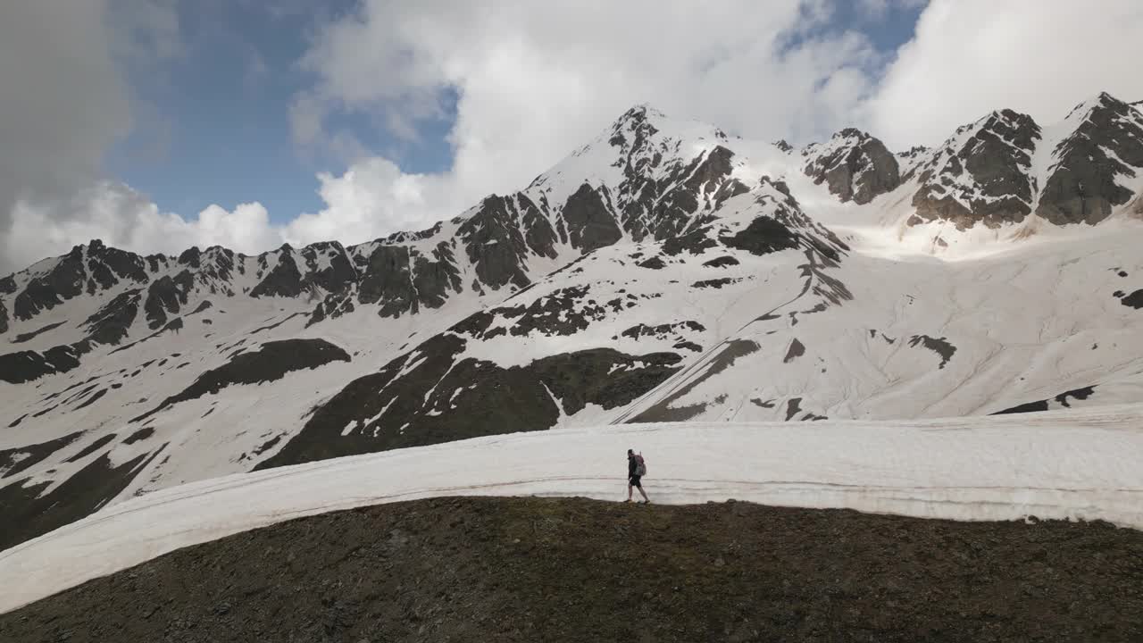 背着背包在斯瓦涅季山区徒步旅行的男子。白雪覆盖的山峰，崎岖的地形。独自旅行者探索，攀登高海拔的小径。冒险，徒步旅行，自然，荒野，挑战，男性启蒙。视频素材