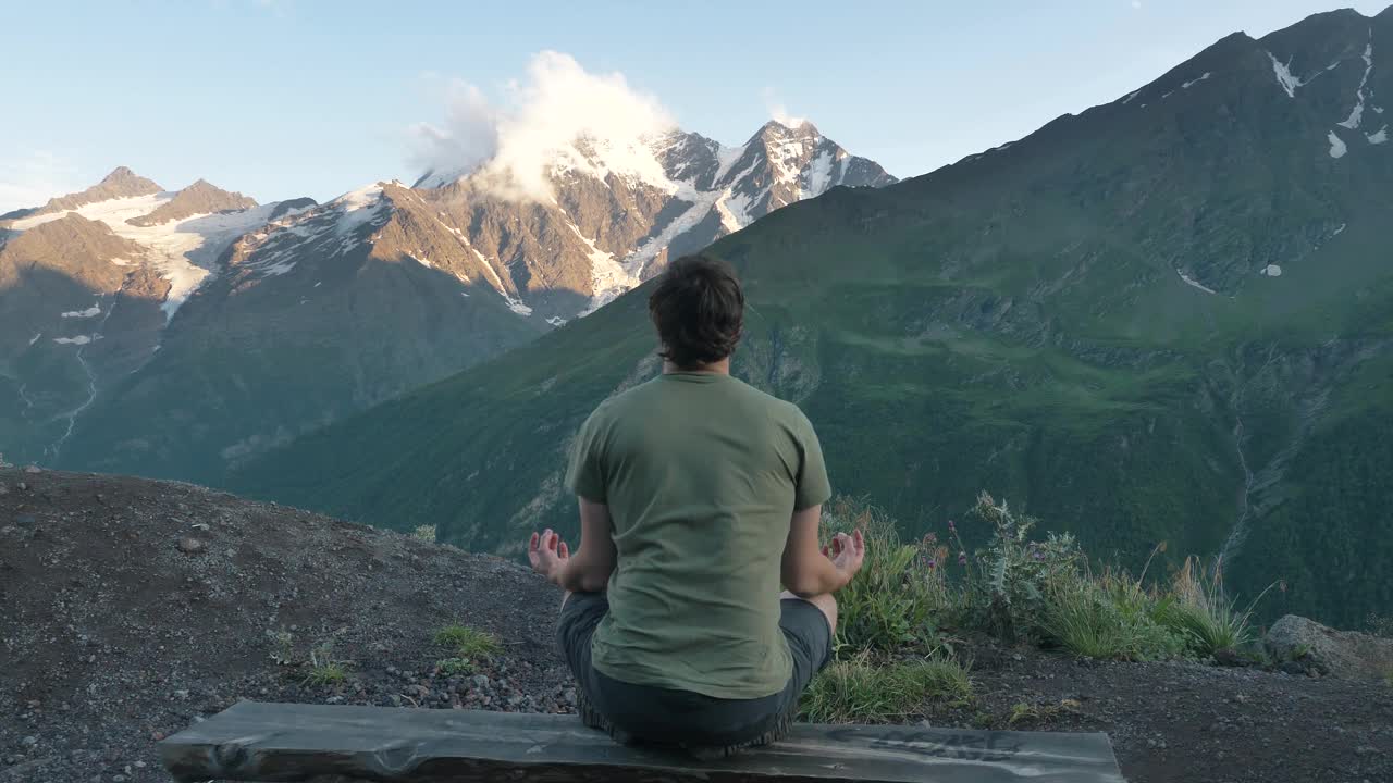 男子以莲花的姿势坐在群山的背景下沉思，后视图视频素材