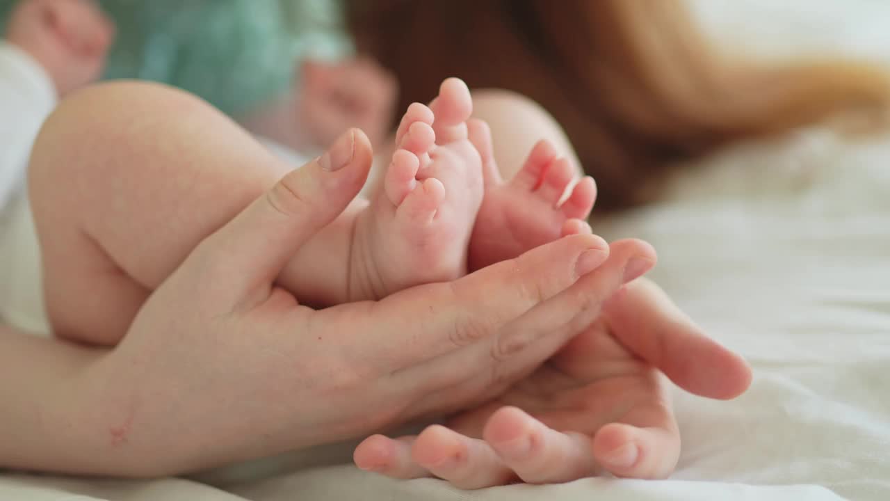 幸福的家庭。刚出生的小男婴或女婴的脚在母亲的手上。母亲抱着刚出生的孩子。妈妈和她的孩子。母性柔情亲子新生活理念。小心轻放。视频素材