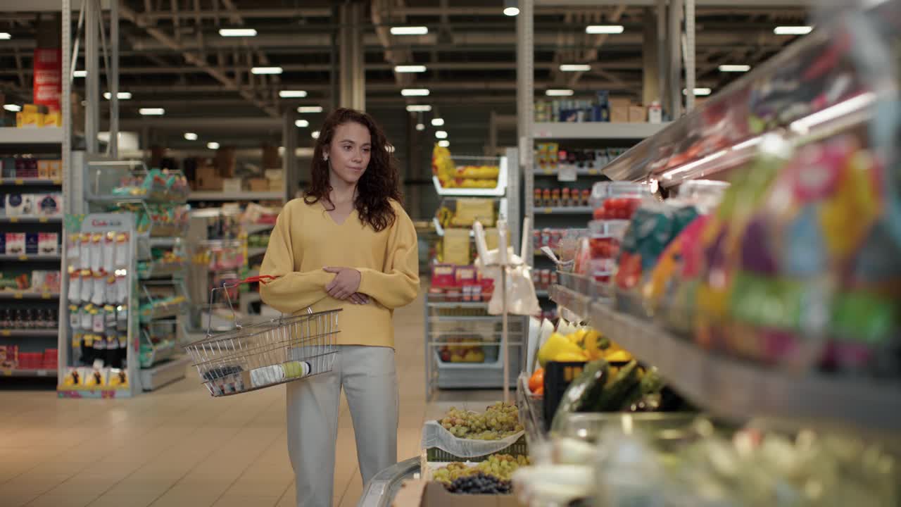 一名年轻女子在超市健康食品区拿着货架上的圣女果和新鲜浆果，拿着购物篮购买食品视频素材