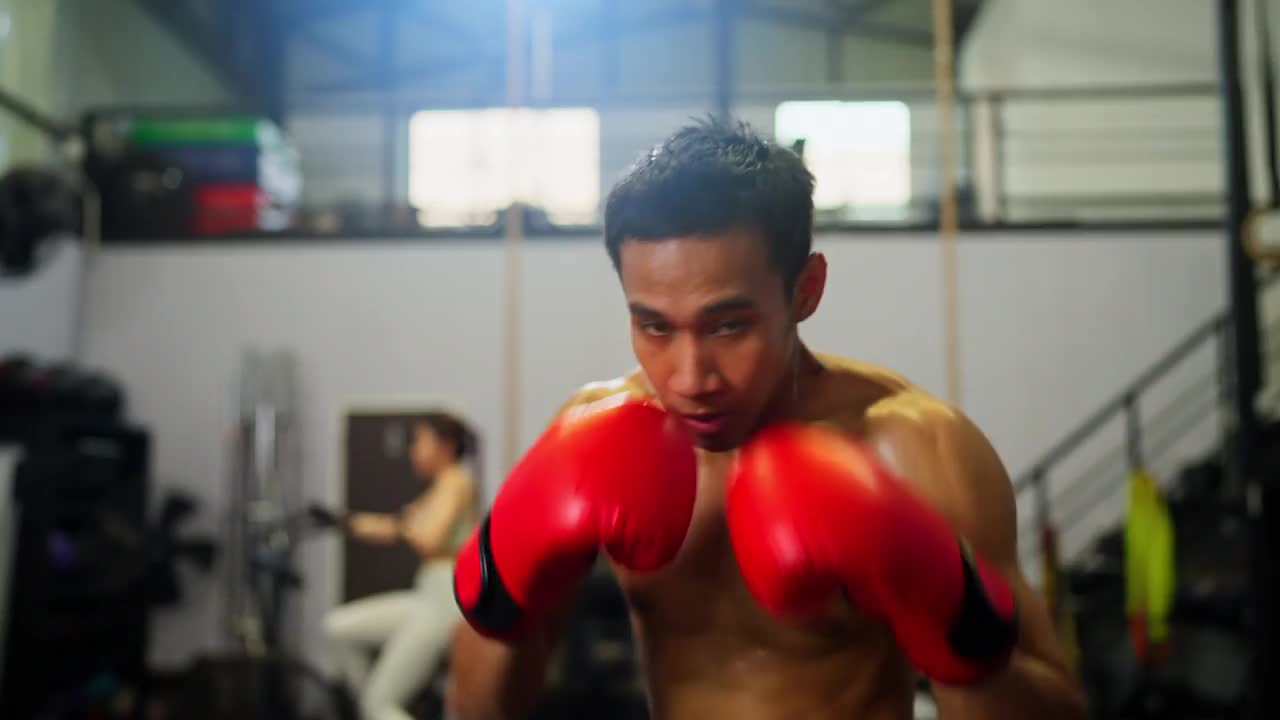 亚洲运动男子戴着红色拳击手套，在体育馆里练习太极拳，她看起来很专注，为了身体健康而练习。视频素材