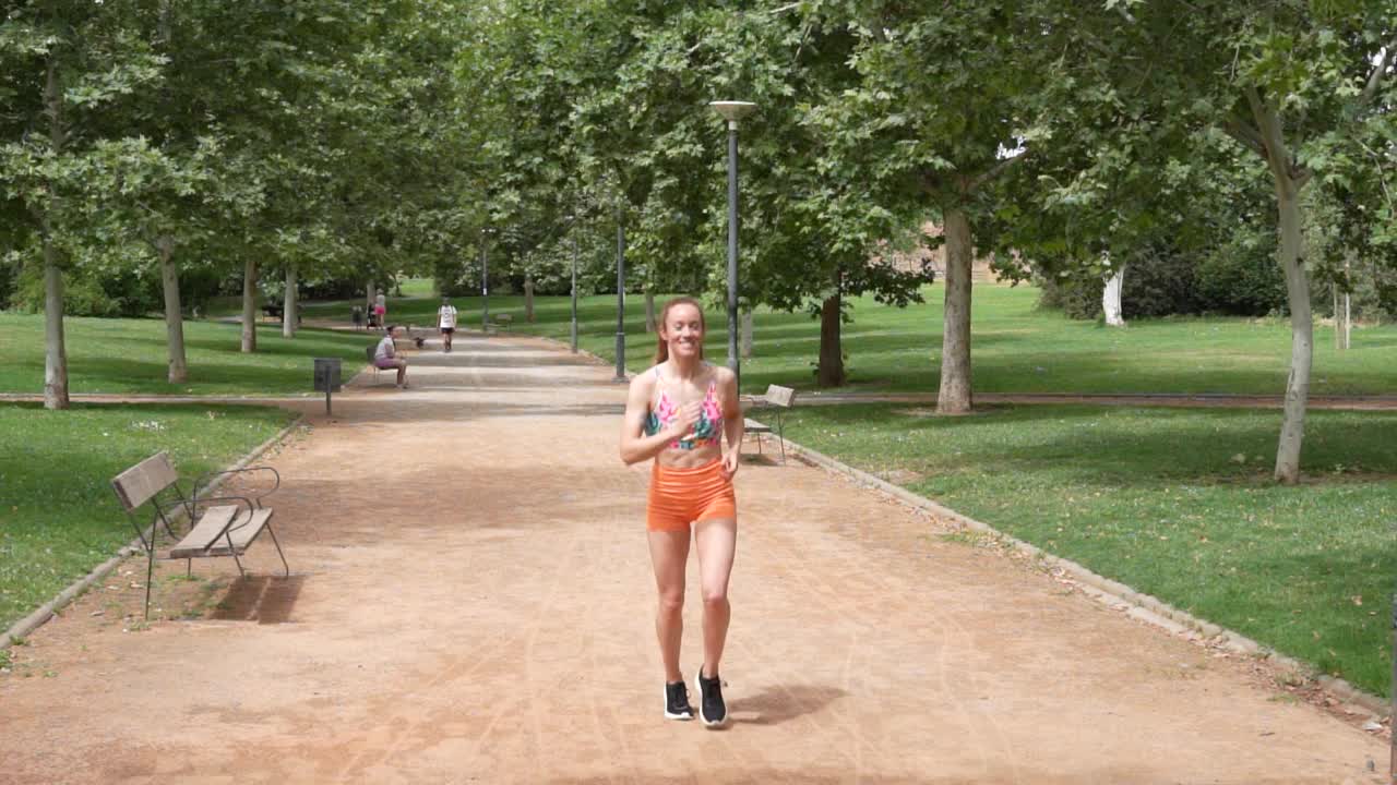 在一个阳光明媚的日子里，一位年轻女子在公园里愉快地慢跑，沉浸在大自然和她的健身计划中视频素材