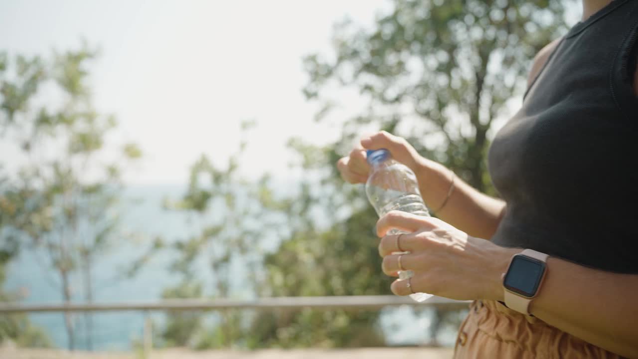 晴天水合，一名年轻女子在户外喝水。明亮的阳光为清新的体验增添了温暖。视频素材