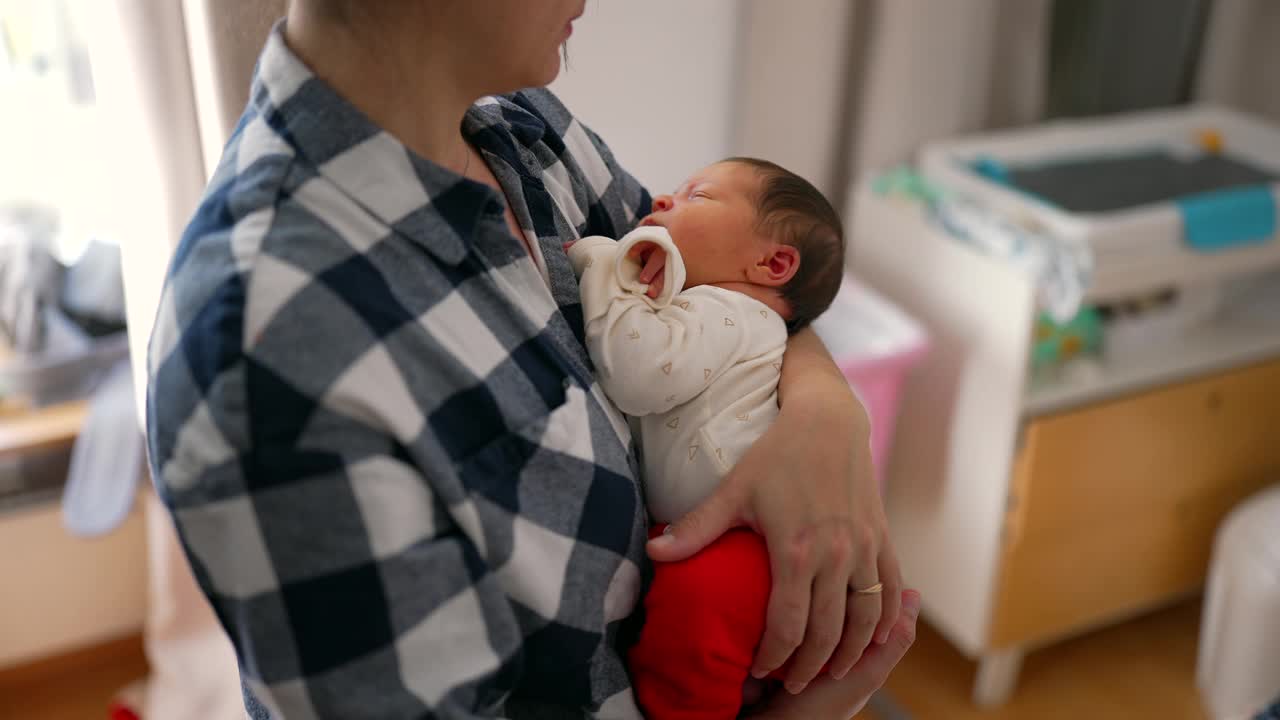 刚出生的婴儿舒适地依偎在母亲的怀里，凝视着母亲。卧室的设置增加了亲密和温柔的气氛视频素材