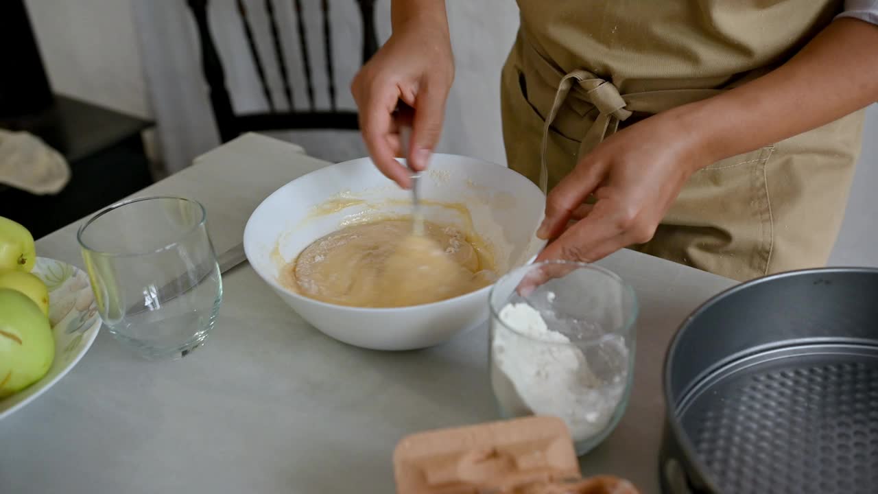 在厨房的工作台上，一个人在一个白色的碗里混合苹果派的面糊和配料视频素材