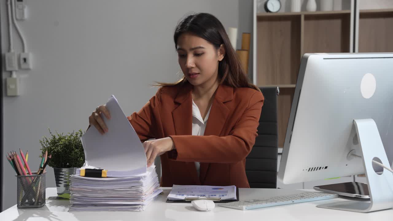 一位亚洲女商人坐在桌旁，面带微笑地工作。她热情地管理着自己的在线酷亚业务，在高效地处理任务的同时，展示了她的奉献精神和积极的态度。视频素材