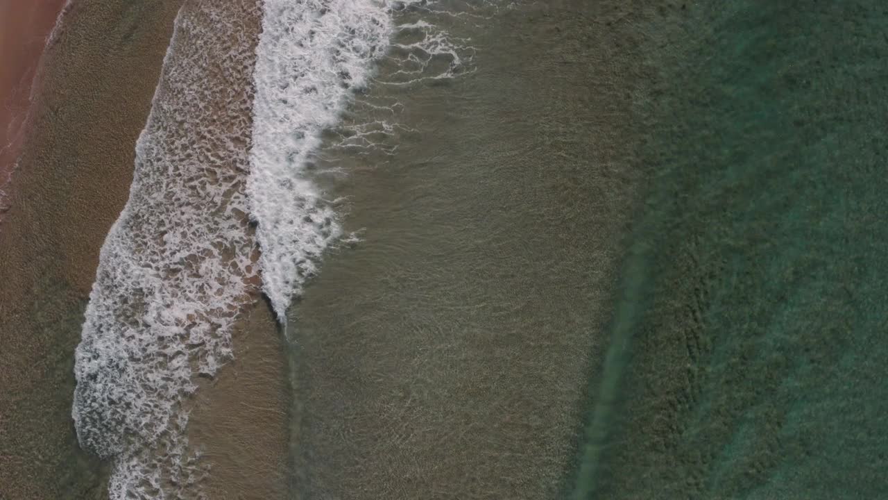 多个干净的海浪沿着清澈、浅、沙质的海岸线破碎，创造出抽象的移动海洋泡沫纹理。在沿着海滩飞行时拍摄的实时照片。视频下载