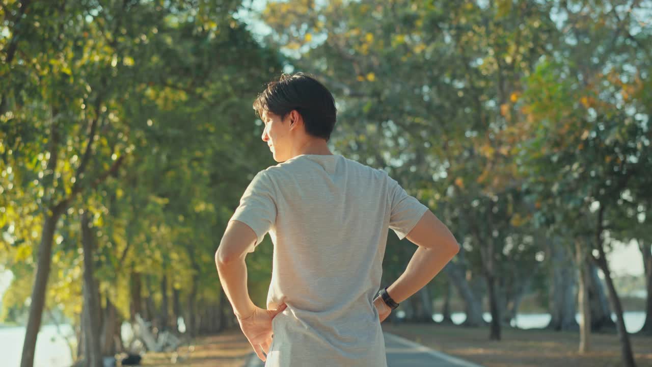 有吸引力的亚洲男子慢跑在公园的树与阳光的背景，健身男子跑步，训练跑步锻炼。视频下载