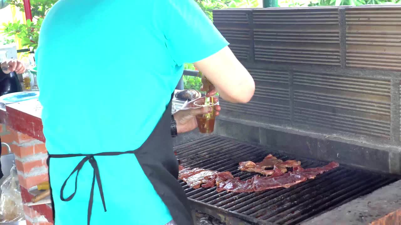 穿着蓝衬衫的人在砖砌背景的烧烤架上烤肉。视频素材