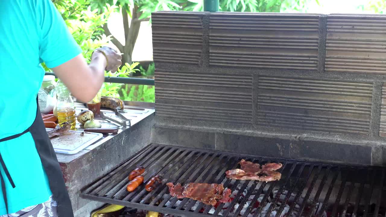 在烤肉架旁边准备食物的人，烤肉和香肠正在烹饪。视频下载