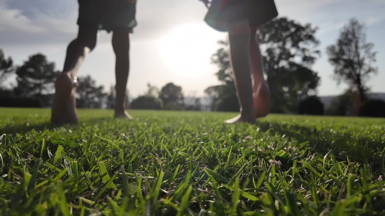 黄昏时，两个赤脚的孩子在草地上奔跑。童年和自由，自由时间玩耍和健康的生活方式在自然环境，户外。视频下载