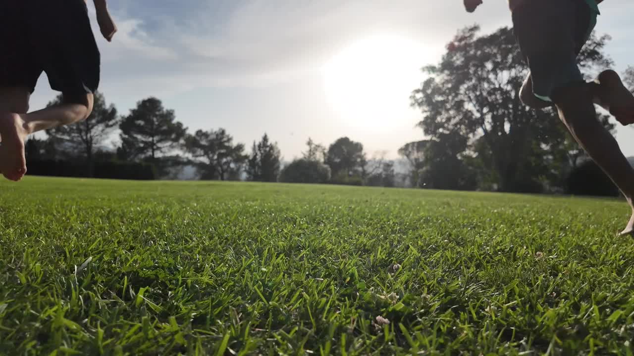 黄昏时，两个赤脚的孩子在草地上奔跑。童年和自由，自由时间玩耍和健康的生活方式在自然环境，户外。视频下载