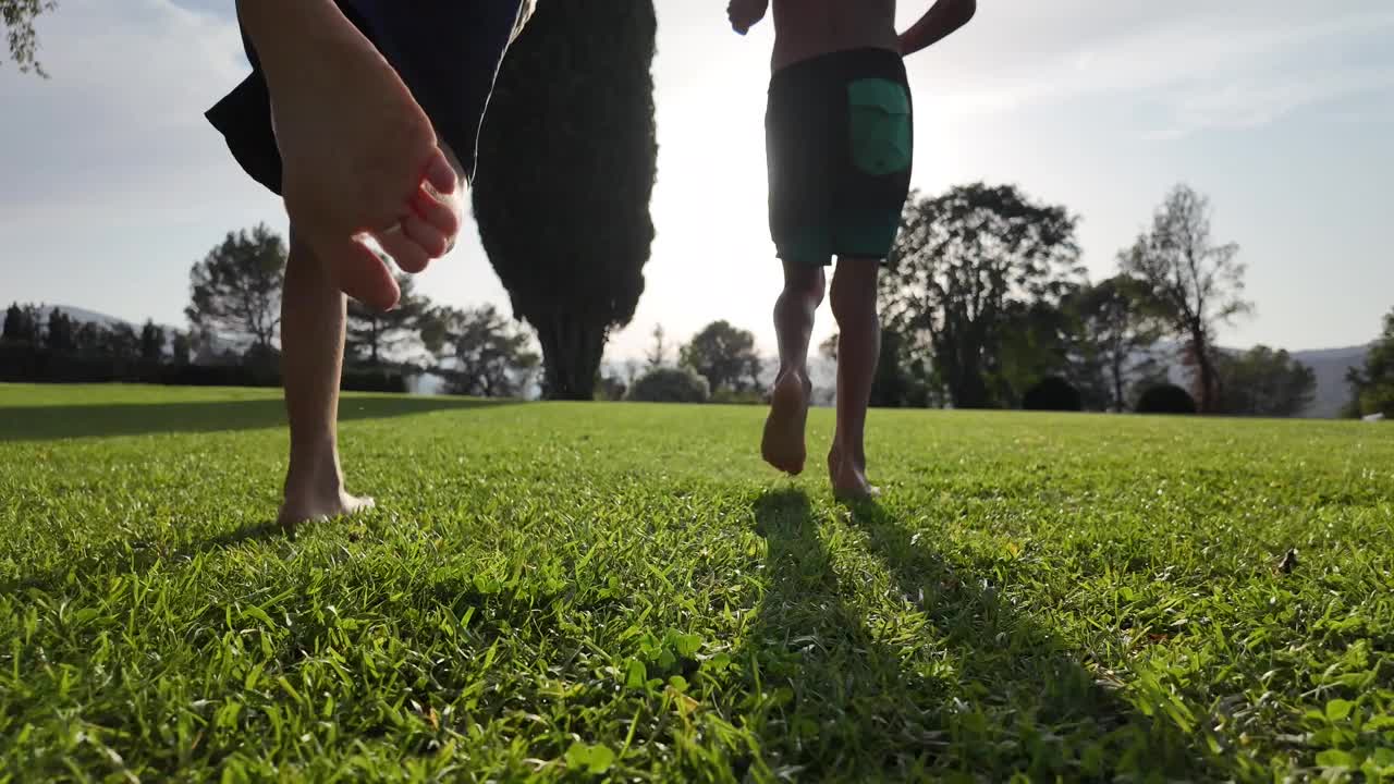 黄昏时，两个赤脚的孩子在草地上奔跑。童年和自由，自由时间玩耍和健康的生活方式在自然环境，户外。视频素材