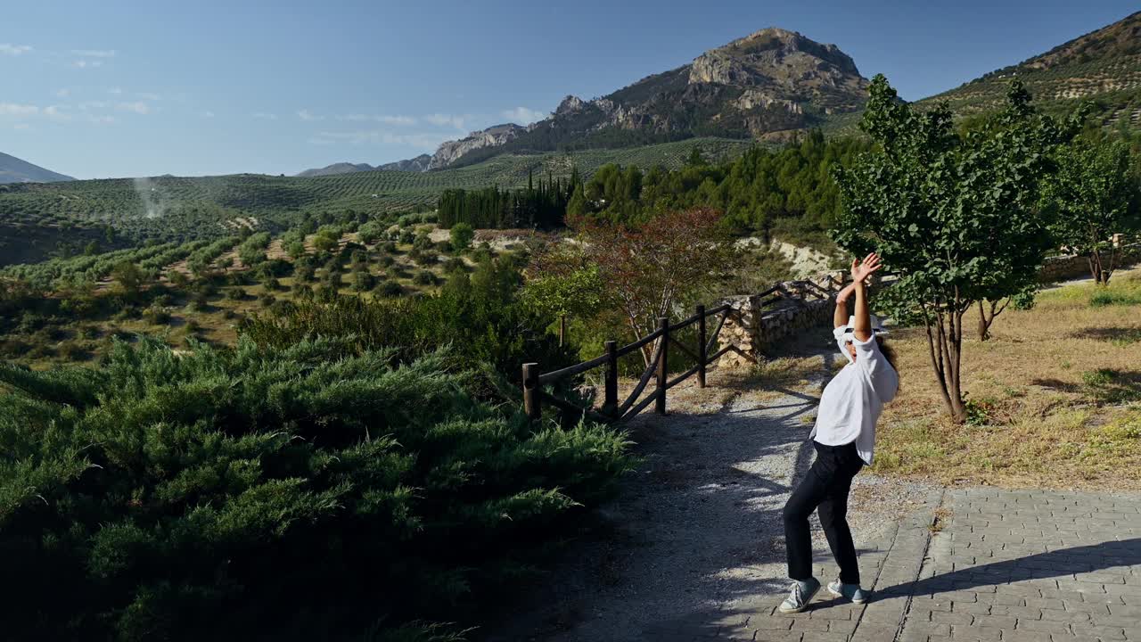 男子在蓝天下的群山和橄榄树林中，在美丽的乡村风景中跳舞视频素材