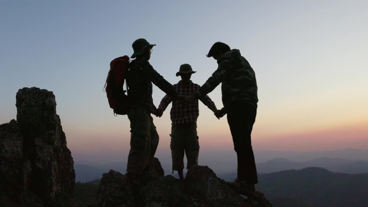 一群登山者在山顶上手拉手的剪影代表了团结和团队合作，成功的理念。视频下载