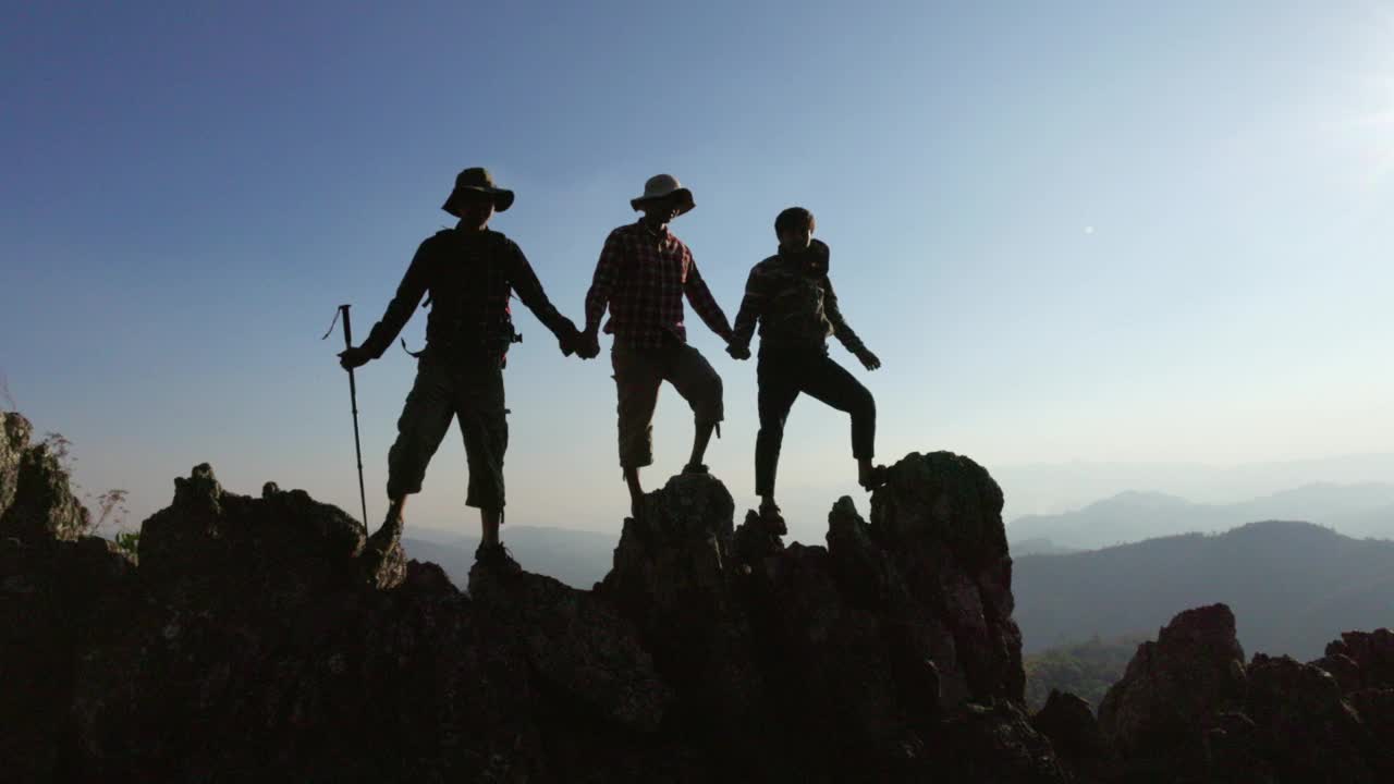 一群登山者在山顶上手拉手的剪影代表了团结和团队合作，成功的理念。视频下载