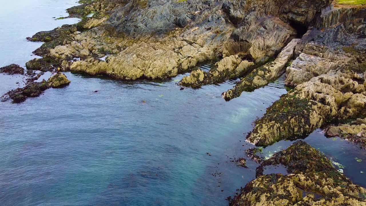 大海是平静的，岩石是锋利的。这水有一种浓郁的蓝色。苔藓和海藻覆盖了岩石。视频素材