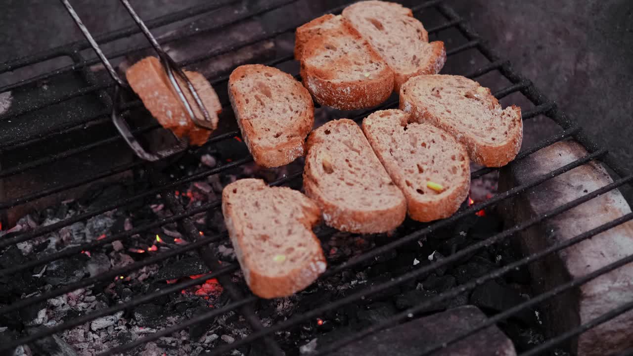 在户外烤架上烤的白面包。在外面野餐。用铁钳把炸好的面包片翻过来。视频下载