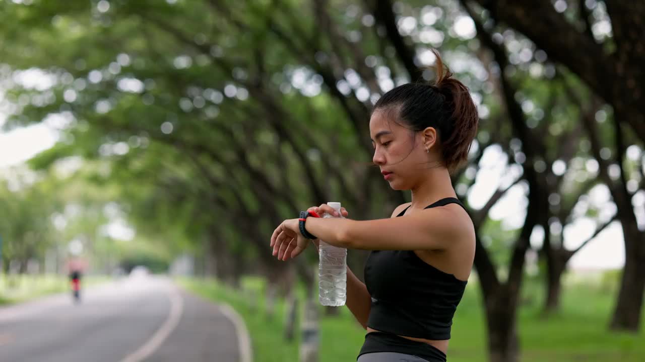 一位亚洲妇女站在那里，喝着瓶装水，在慢跑后放松一下。视频素材