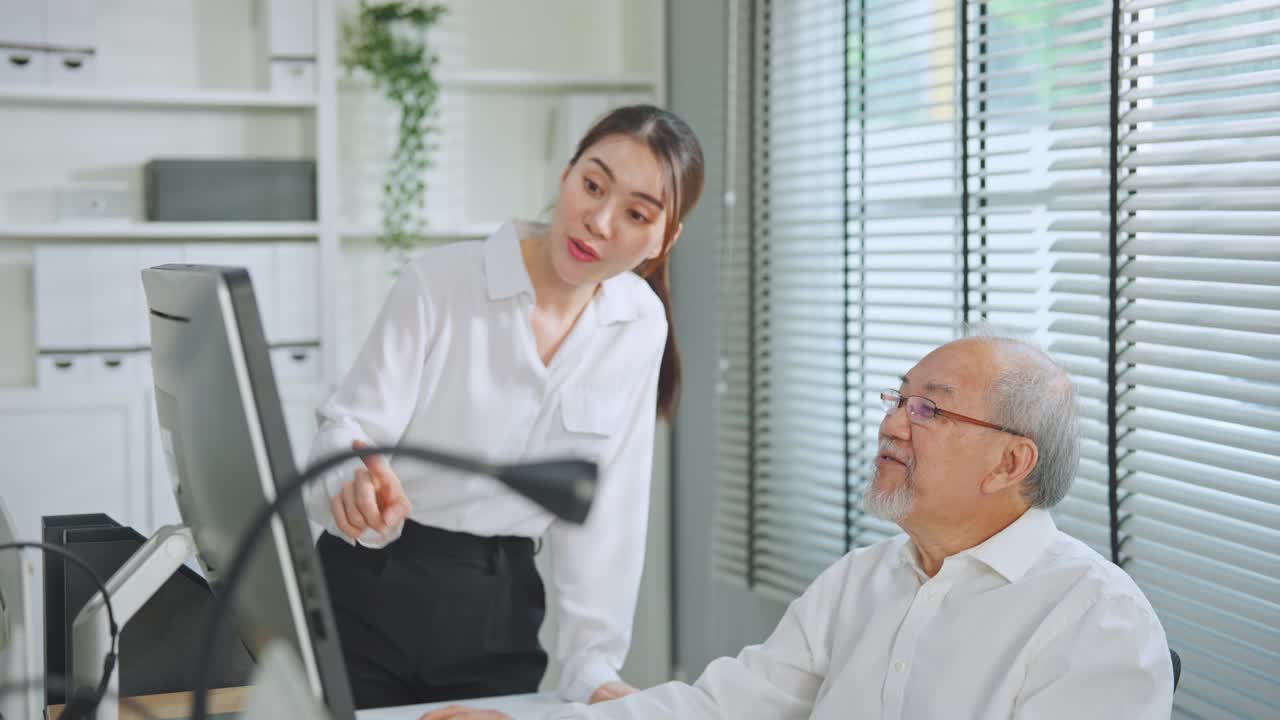 在办公室工作的亚洲资深商人和行政女性。有吸引力的年轻女商人帮助和支持成熟的员工同事在现代企业工作场所的设备上做项目。视频素材