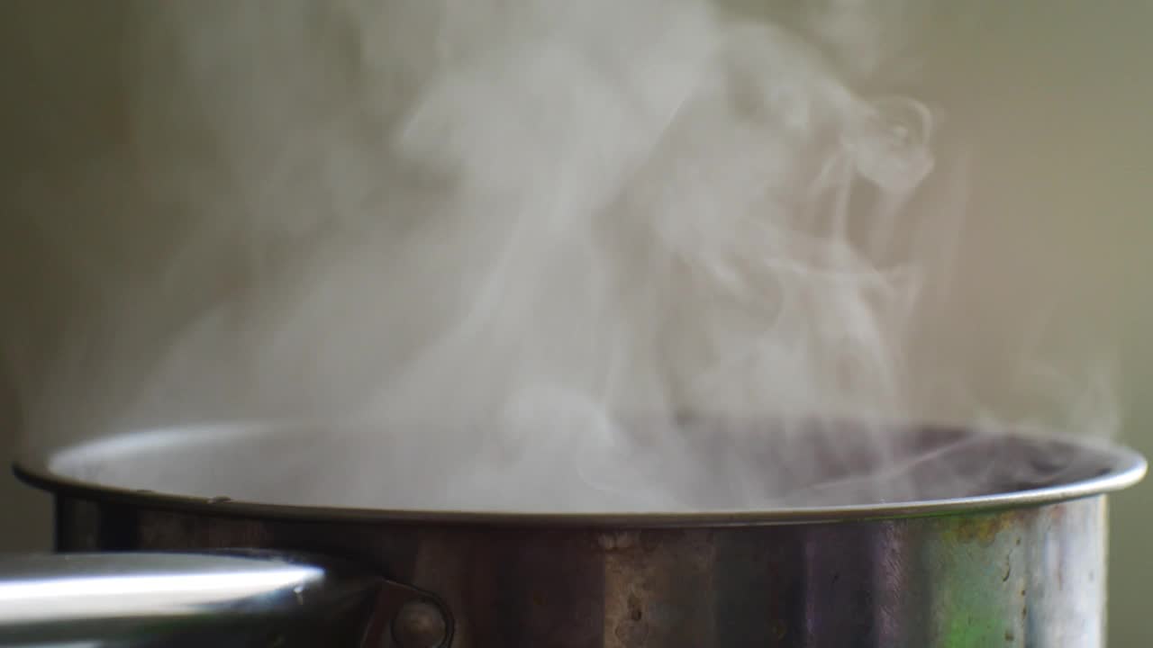 食物是在不锈钢锅里炖熟的。女孩用勺子做圆周运动慢慢搅拌。侧面特写。到处都是蒸汽视频下载