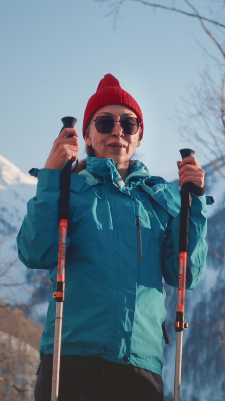 在冬天的山上徒步旅行的老妇人。一位老妇人拄着拐杖进行越野行走。白雪皑皑的山峰。视频下载