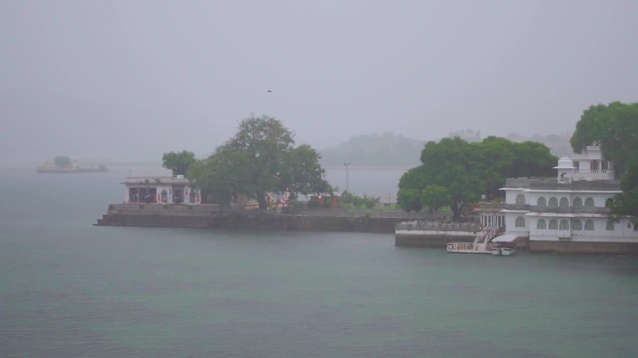 大雨中的乌代浦尔市和皮丘拉湖的慢镜头。季风季节，大雨落在湖面上。印度拉贾斯坦邦乌代普尔的Ambrai Ghat白天倾盆大雨。视频下载