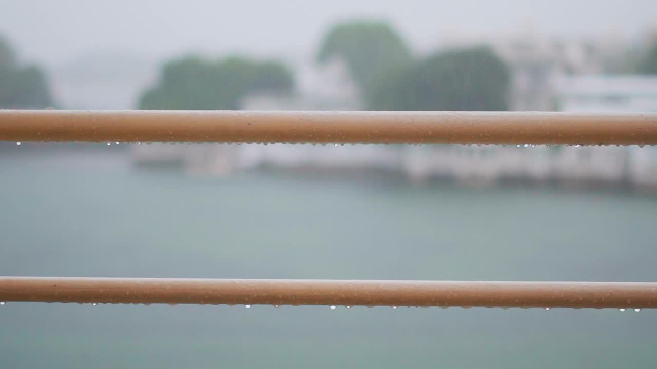 雨滴落在金属栏杆上，背景是雨水。雨季，印度拉贾斯坦邦乌代普尔的皮丘拉湖。在雨季旅行。视频素材