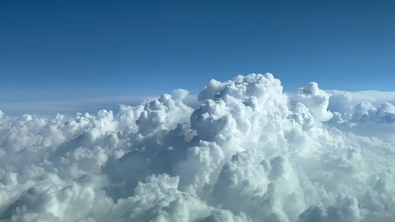 从巡航水平的飞机驾驶舱拍摄的一个巨大的暴风雨云的顶部附近的POV，阳光明媚的蓝天。4 k 60 fps视频素材