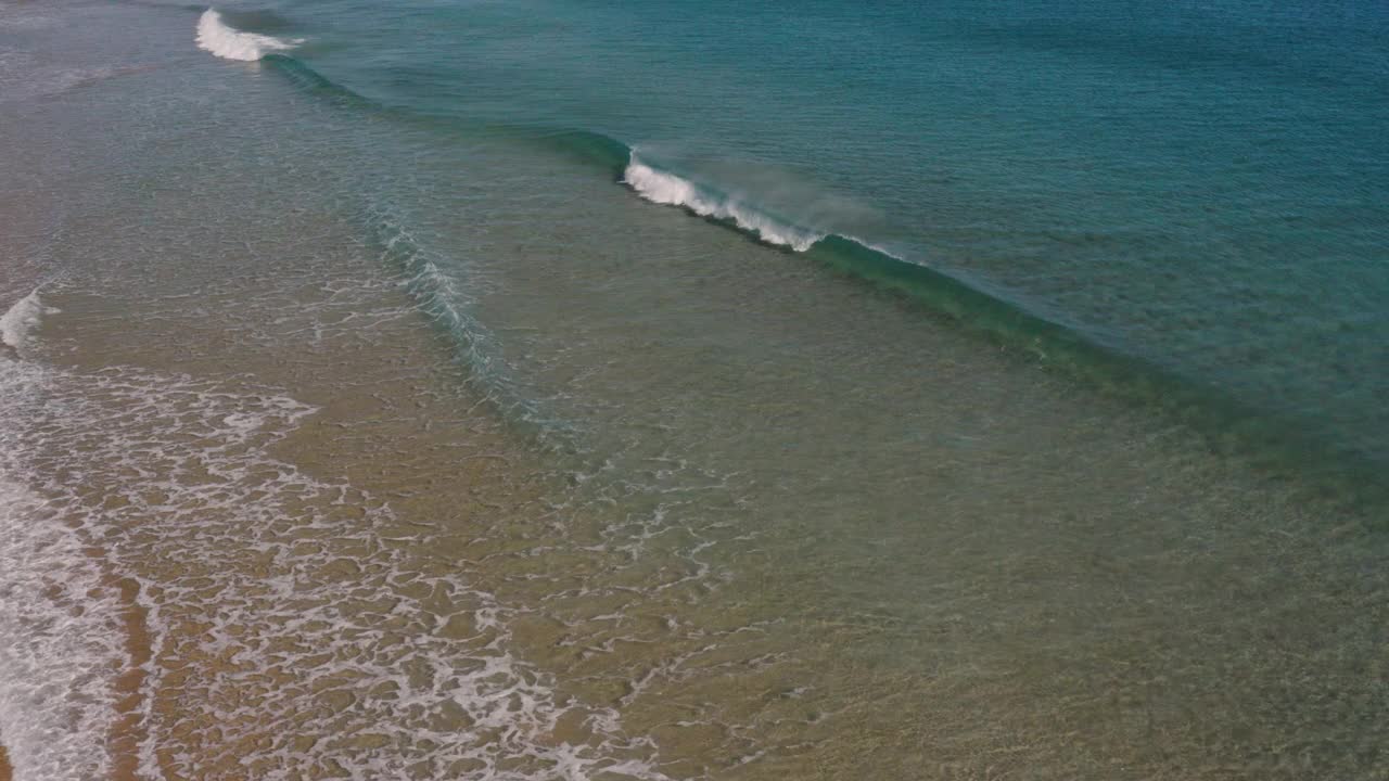 鸟瞰图美丽的绿松石水浪打破沿着田园诗般的清澈，浅，沙滩海岸线。视频素材