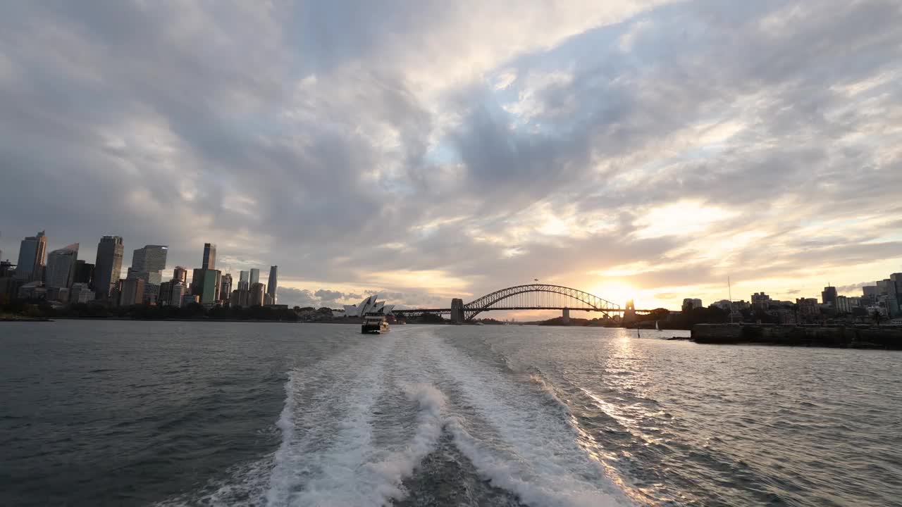 日落时分在海港区从客船上俯瞰悉尼歌剧院，背景是城市天际线和海港大桥视频下载