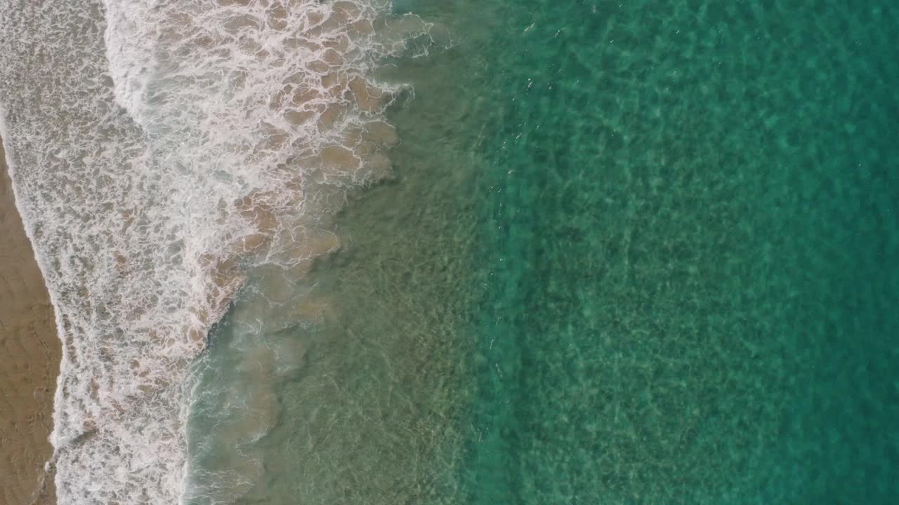 鸟瞰图美丽的绿松石水浪打破沿着田园诗般的清澈，浅，沙滩海岸线。视频下载