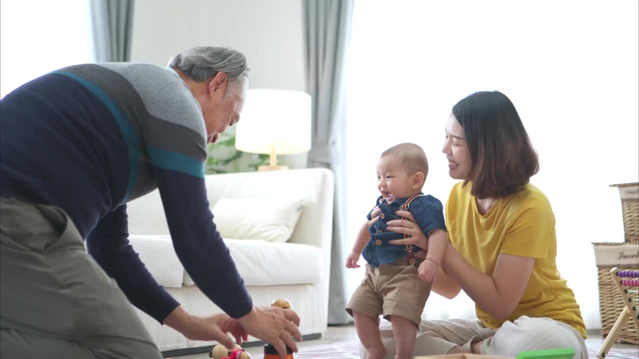 一个小孩子和妈妈、爷爷在客厅的地板上愉快地玩着玩具视频素材