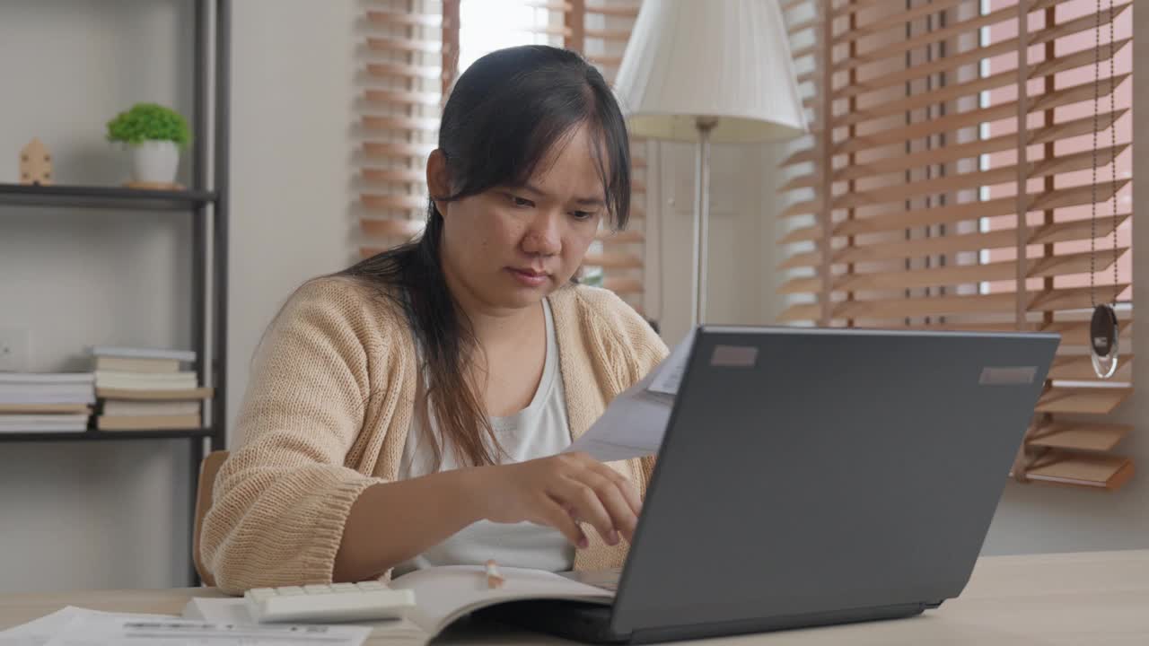 一位忧心忡忡的亚洲妇女正在用笔记本电脑计算家庭财务账单视频素材