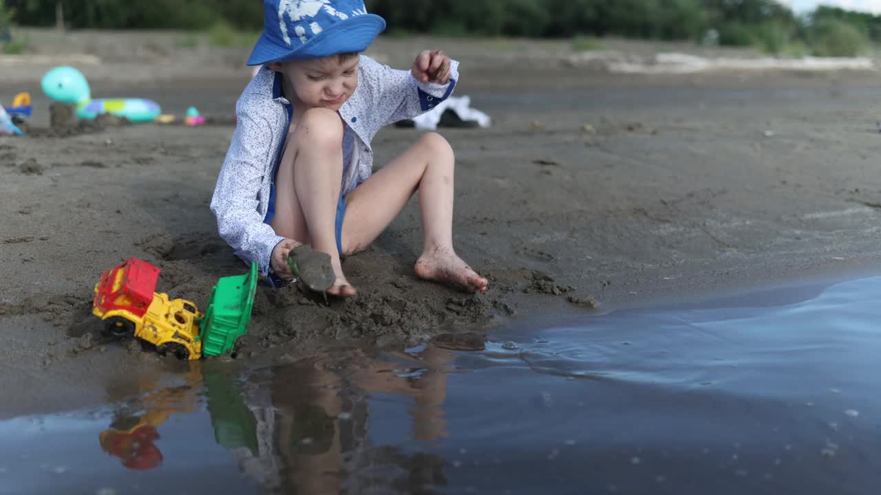 一个小孩子在明亮的阳光下快乐地在海滩上玩着五颜六色的玩具视频下载