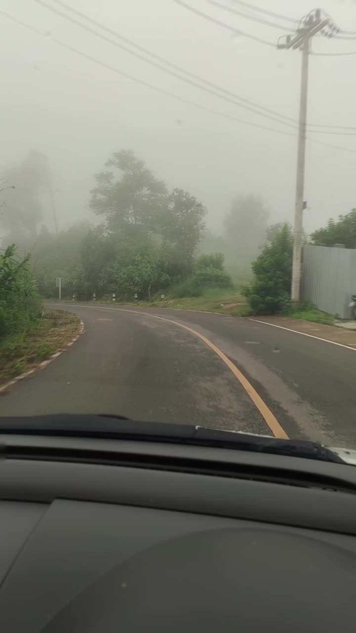 从汽车挡风玻璃上拍摄的一条雾蒙蒙的乡村道路，展示了树木、电线和雾蒙蒙的气氛。视频下载